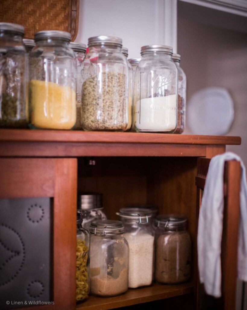 A pantry cabinet filled with glass jars of dry goods inside & on top!