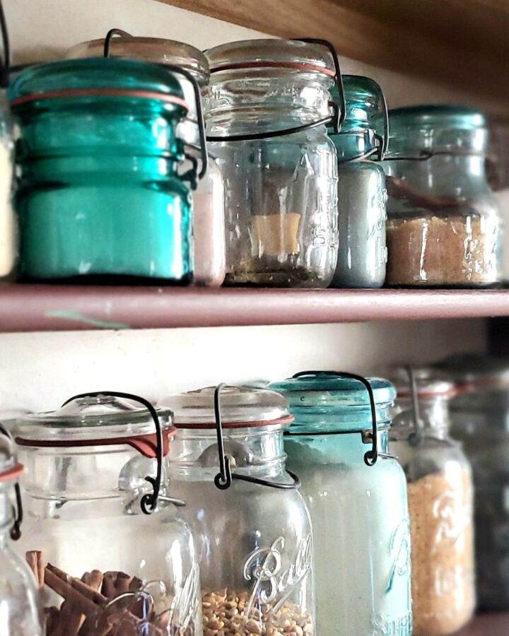A two tiered wall shelve with a variety of Vintage mason jars filled with dry goods.