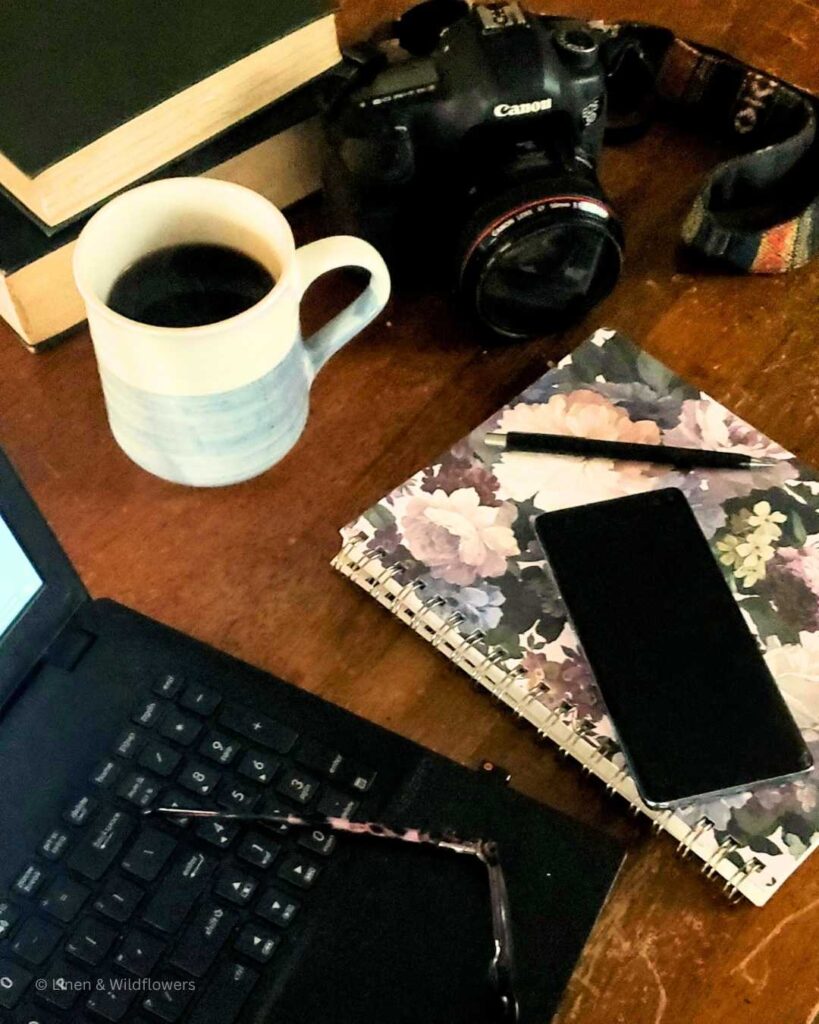To old books for reference for blogging, a canon camera, cup of black of coffee. cell phone & a black pen o a flowered notebook.