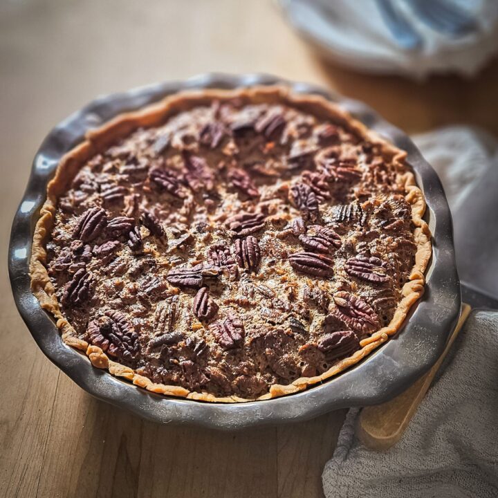 A freshly baked old-fashioned Southern Pecan Pie in a stone pie dish cooking on the butcher block.
