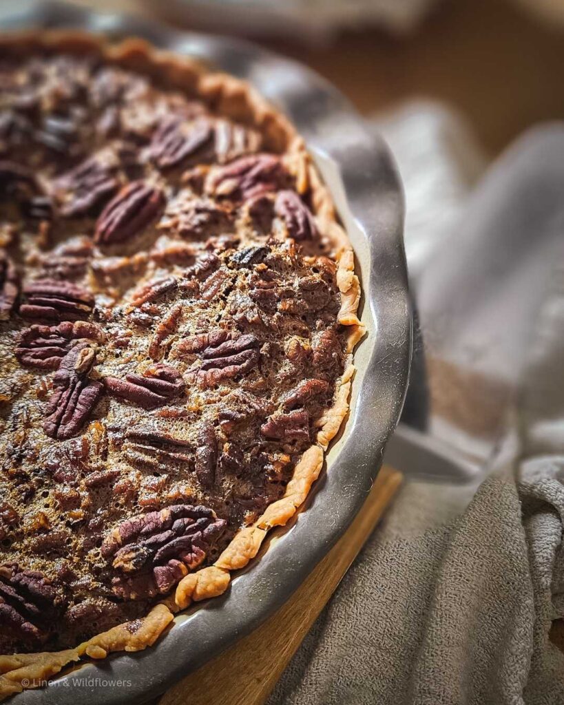  a freshly baked Old-Fashioned Southern Pecan Pie in a stone pie plate cooling on a butcher block.