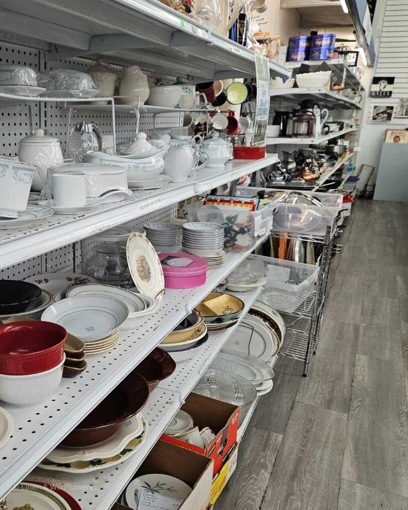 Thrift store shelves filled with a variety of dishes & cookware.