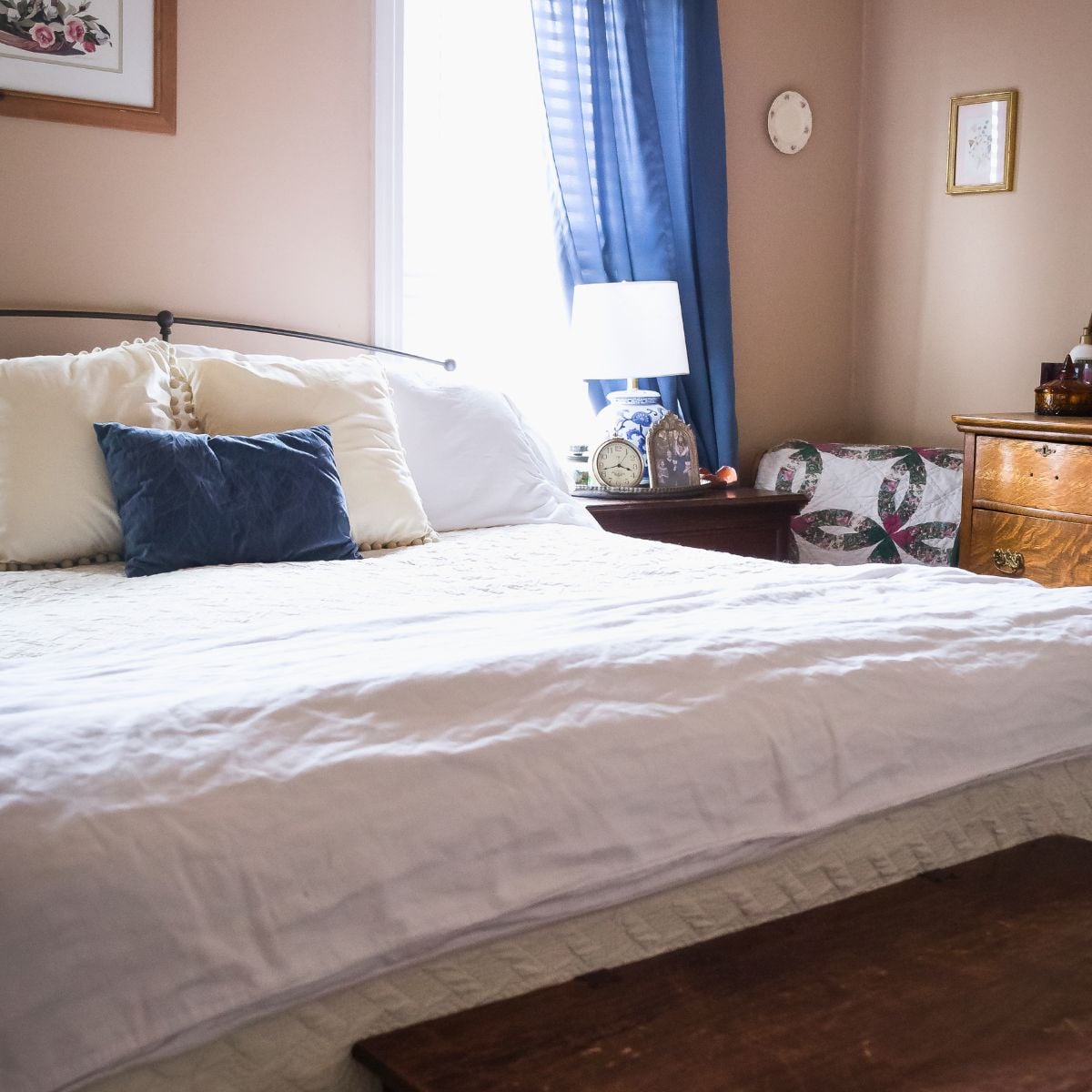 Bed with white bedding and a blue velvet pillow in a vintage bedroom, showing why a mattress protector pad is essential.