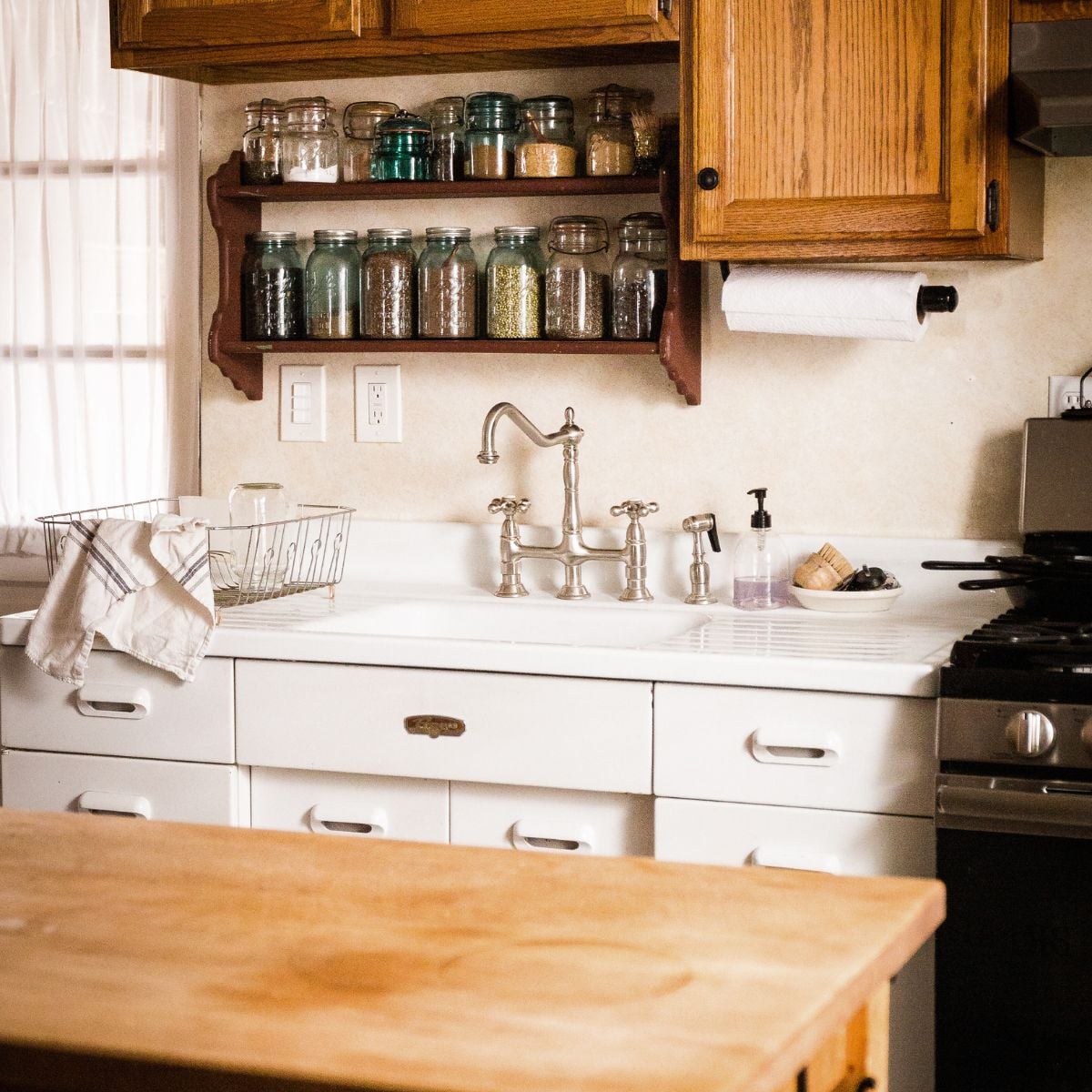 Farmhouse kitchen with a wall shelf of antique blue canning jars filled with pantry staples above a vintage drainboard sink.