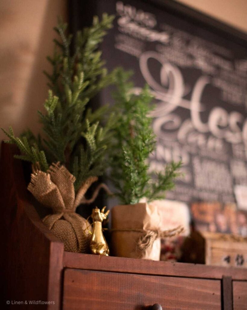 Winter theme faux mini trees on the shelf with a gold deer in front of a large black & white photo.