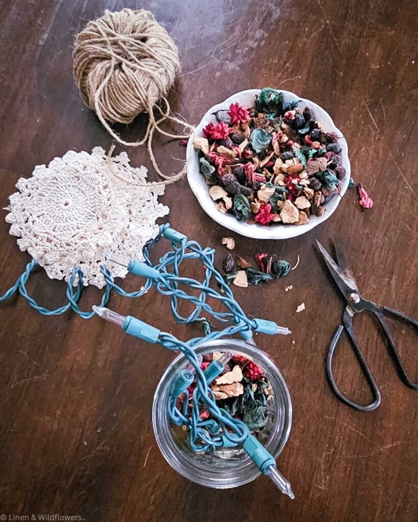 Cozy crafting scene with twine, crochet, a bowl of colorful potpourri, vintage scissors, and tangled fairy lights on a wooden table.