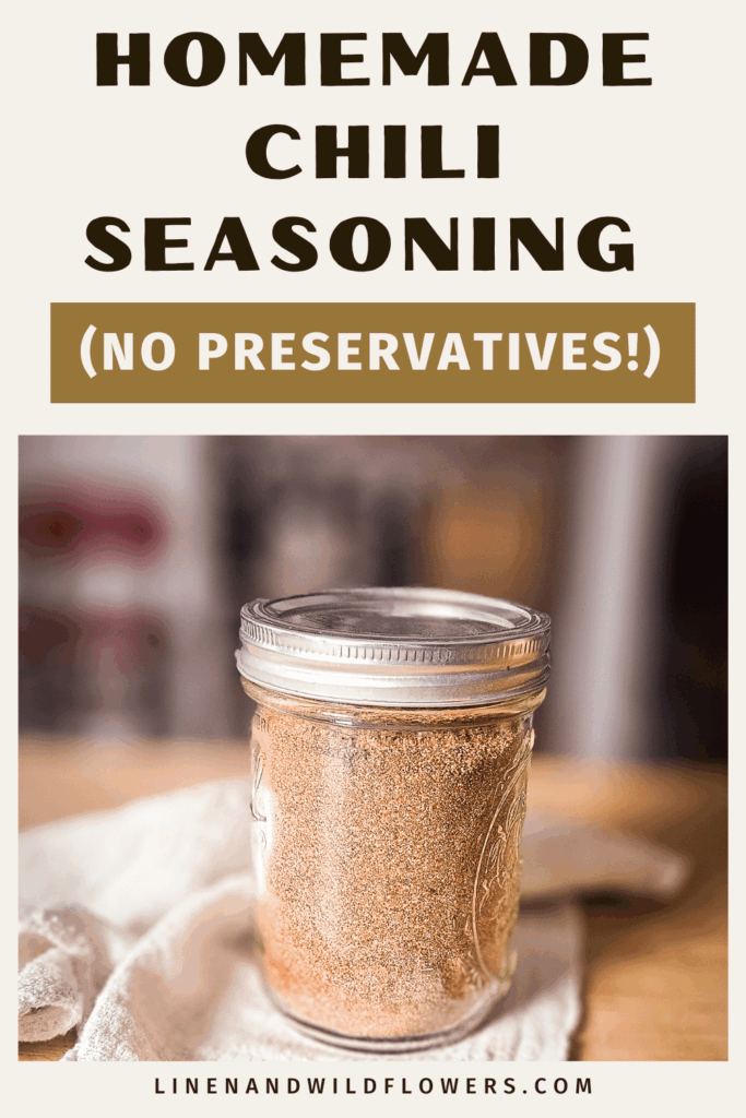 Mason jar filled with homemade chili seasoning sits on a wooden surface. Text above reads "Homemade Chili Seasoning (No Preservatives!)." Cozy, rustic feel.