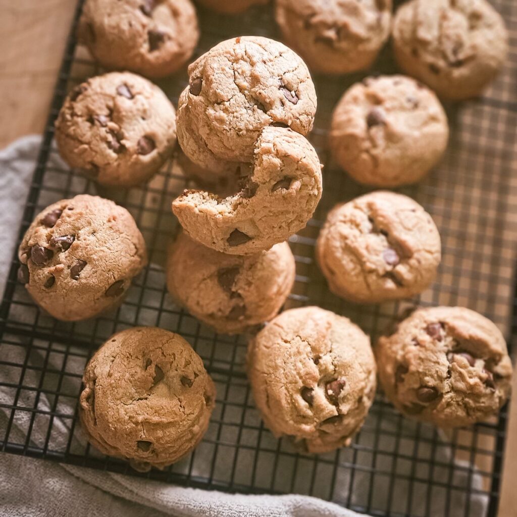 A stack of chocolate chip cookies on a cooling rack, one with a bite taken. Warm tones create an inviting, homemade feel.