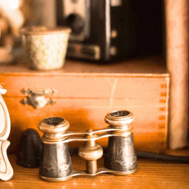 Vintage binoculars glasses with ornate detailing rest on a wooden surface, surrounded by a small ceramic container and a wooden box, evoking nostalgia.