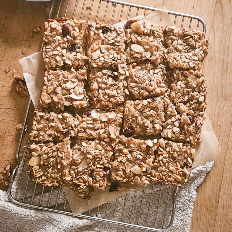 Homemade oat bars with nuts and dried fruit arranged in neat rows on a cooling rack. Placed on parchment paper, the bars convey a cozy, homemade feel.