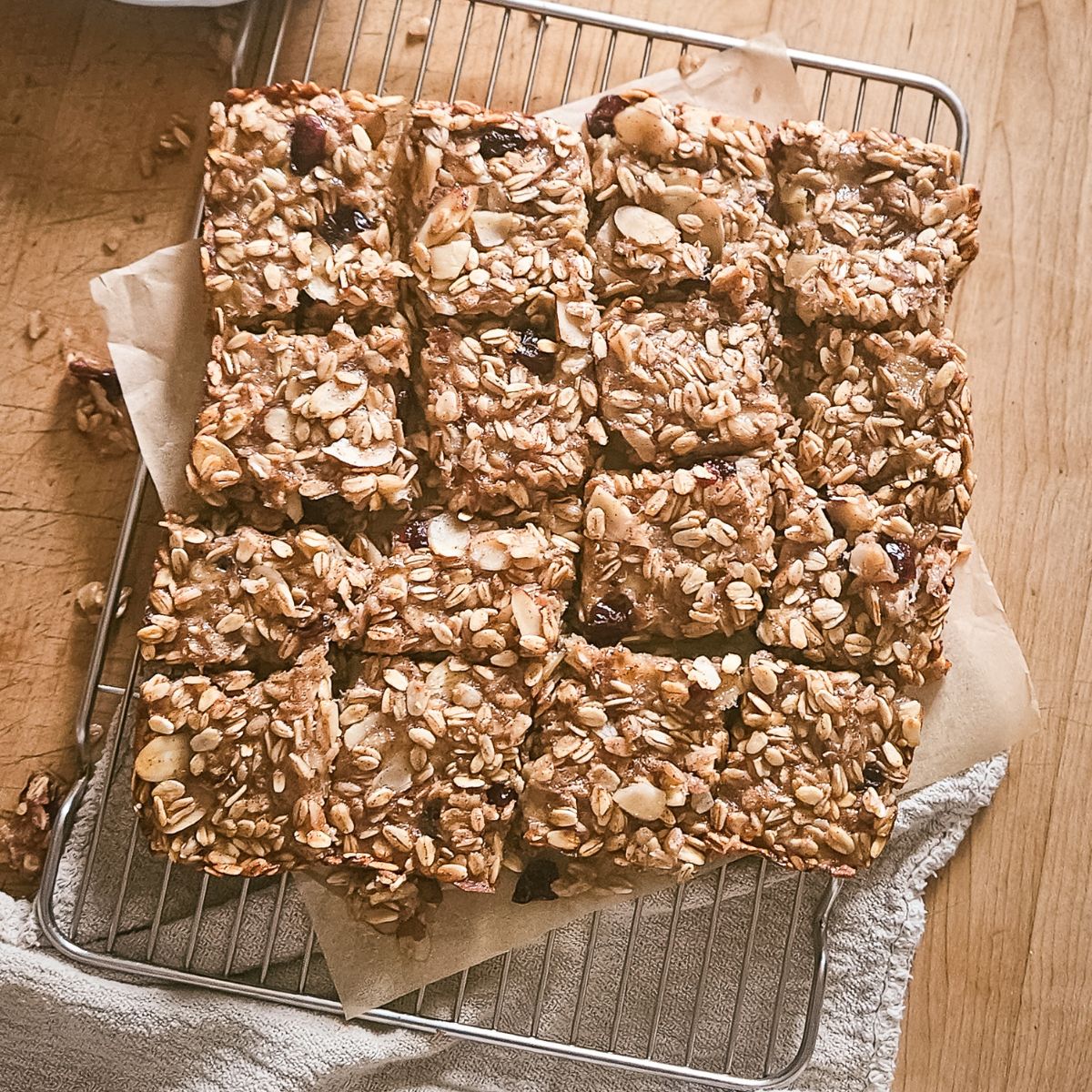 Homemade oat bars with nuts and dried fruit arranged in neat rows on a cooling rack. Placed on parchment paper, the bars convey a cozy, homemade feel.
