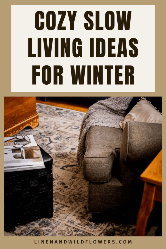 Cozy living room setup with a plush armchair, soft gray blanket, beige pillow, and a rug. A coffee table holds glasses and magazines. Warm, inviting ambiance.