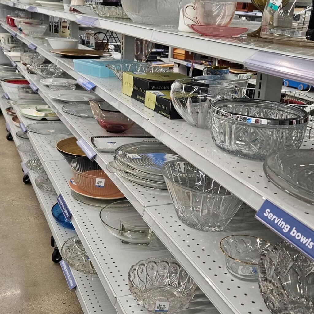Shelves filled with assorted glass and crystal serving bowls and platters in a store. Variety of shapes and sizes, evoking a sense of organized abundance.