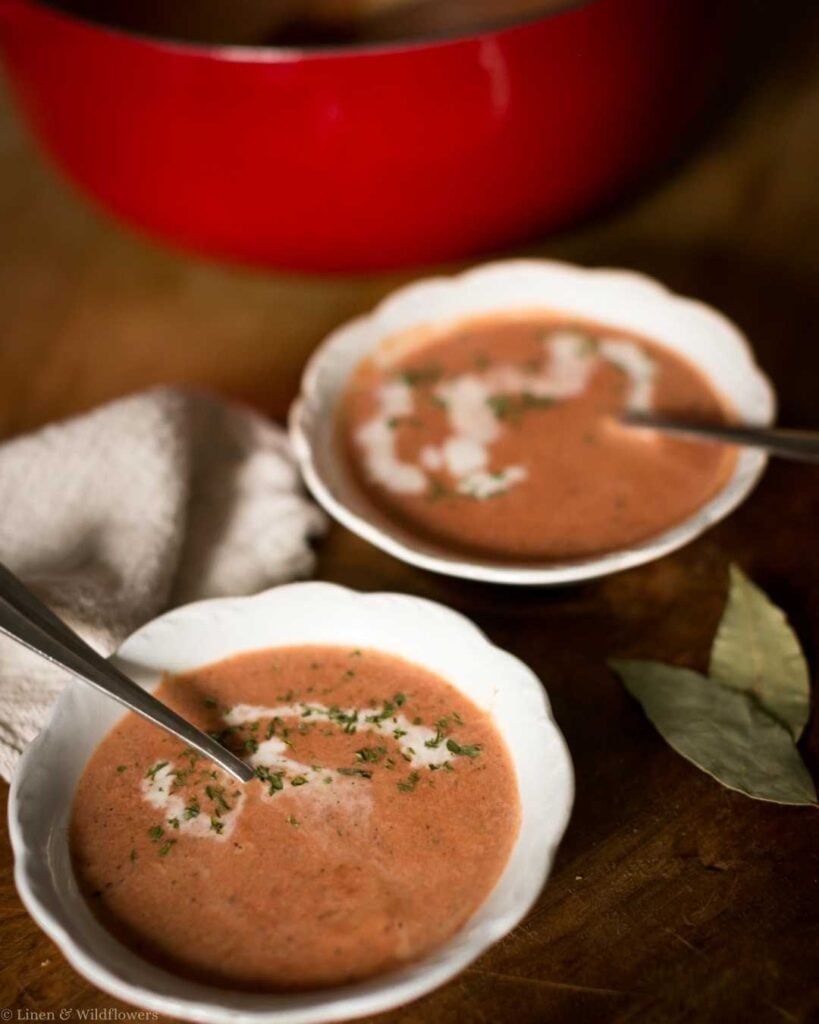 Creamy homemade root blend soup topped with a drizzle of cream and herbs, served in white bowls on a rustic wooden table with a red Dutch oven in the background.