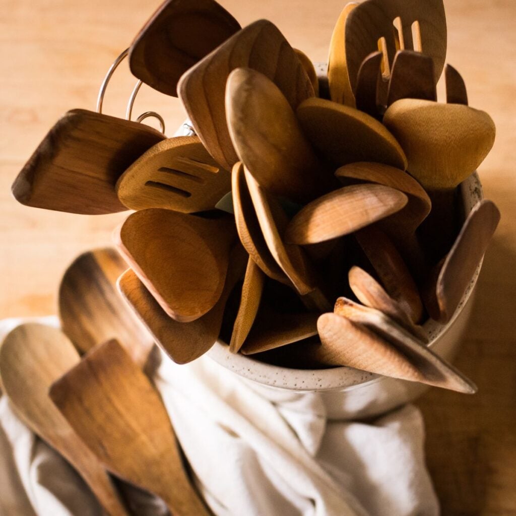 A collection of wooden kitchen utensils, including spoons and spatulas, is gathered in a ceramic container on a wooden surface, conveying warmth and rustic charm.