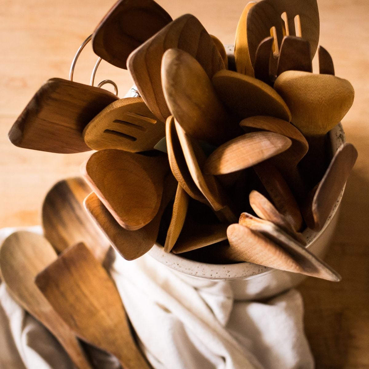 A collection of wooden kitchen utensils, including spoons and spatulas, is gathered in a ceramic container on a wooden surface, conveying warmth and rustic charm.