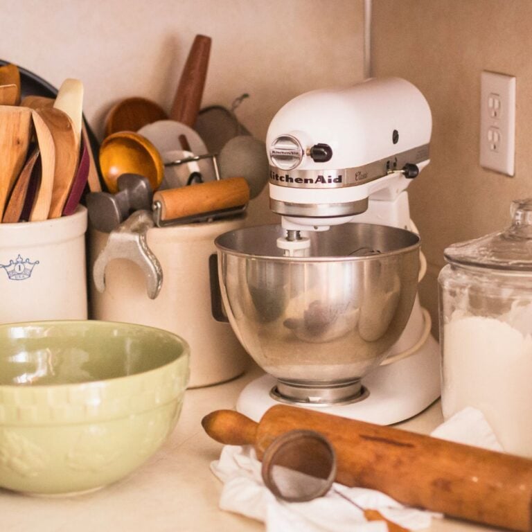 A cozy kitchen corner with a white stand mixer, various wooden utensils in a crock, a rolling pin, and a bowl of flour on the counter.