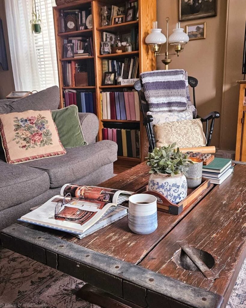 Cozy coffee table styled with thrifted decor, books, a candle, and greenery in a warm living room.