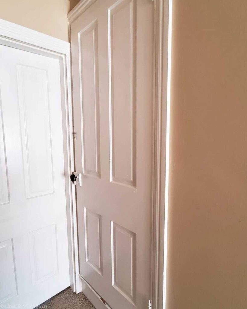 An attic door next to a third-floor bedroom. It has a white, paneled design and a dark handle, creating an awkward architectural feature.