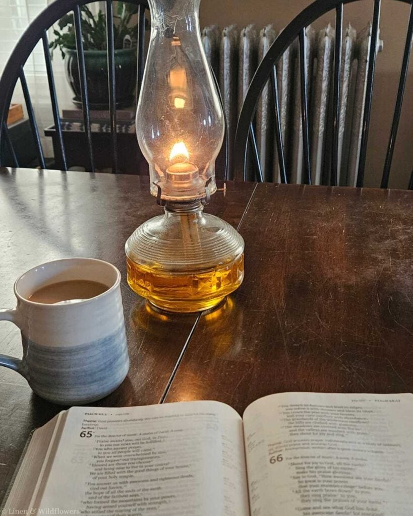 A cozy scene with an open book, a steaming mug, and a glowing oil lamp on a wooden table. The soft light and warm tones suggest relaxation.