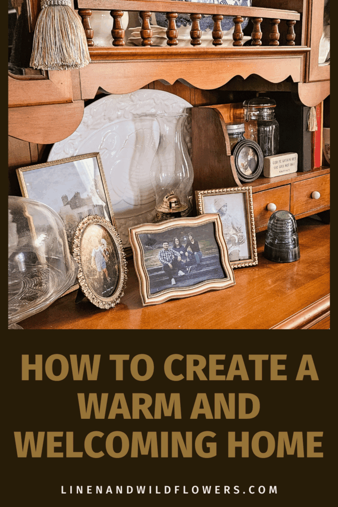 A cozy wooden shelf displays framed family photos and vintage decor, creating a warm, nostalgic atmosphere. Text reads "How to Create a Warm and Welcoming Home."