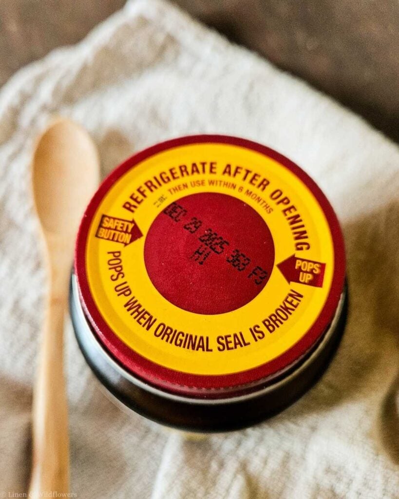 Close-up of an active dry yeast jar lid showing "Refrigerate After Opening" label and expiration date stamp, key to knowing if yeast is expired.
