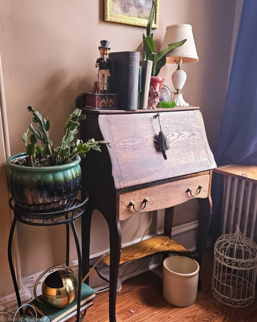 Affordable collected home styling with antique secretary desk, houseplants, and vintage figurine.