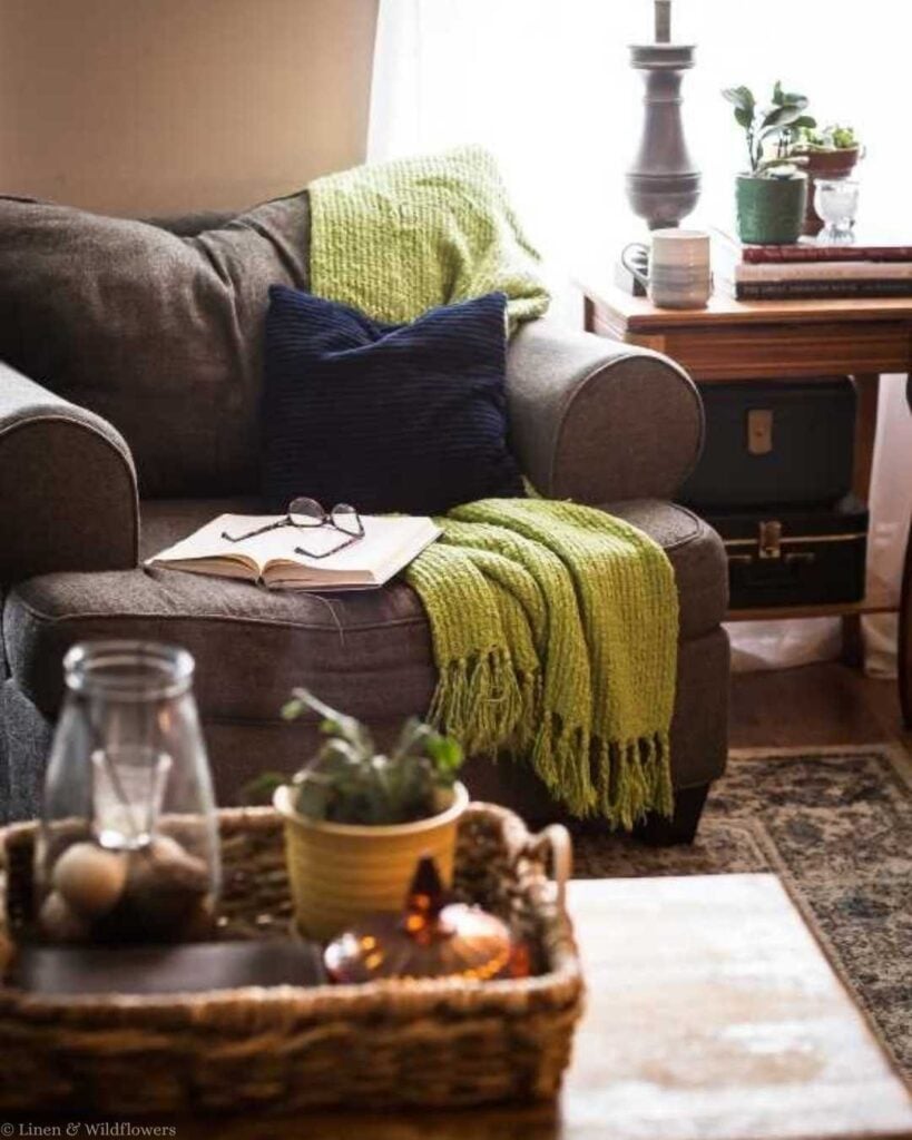 Budget-friendly collected home living room with thrifted armchair, green throw blanket, and reading nook.