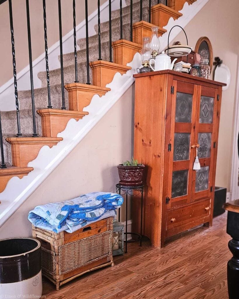 Vintage pie safe cabinet styled under staircase as budget-friendly collected home decor idea.