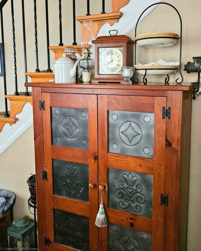 Punched tin pie safe topped with mantel clock and oil lamp, a thrifted find for collected home décor.