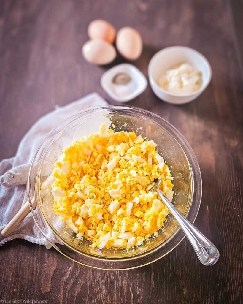 Chopped hard-boiled eggs in a glass mixing bowl with a fork, the first step in making old-fashioned egg salad.
