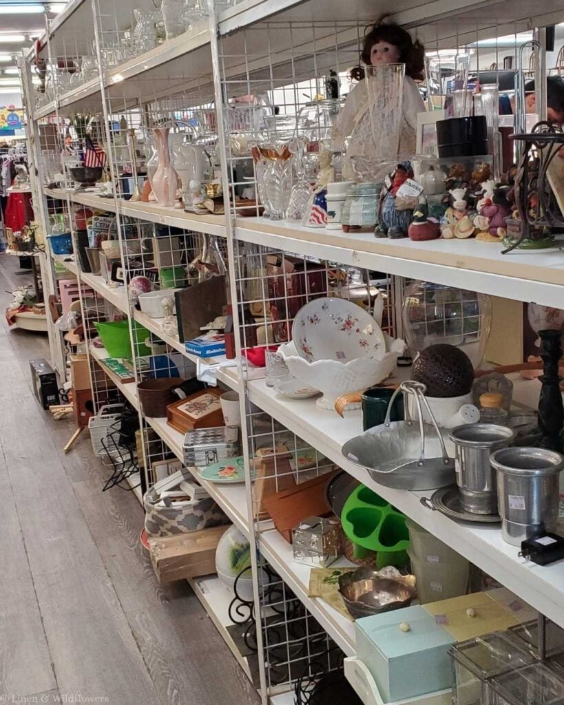 Thrift store shelves lined with secondhand kitchenware, plates, vases, and home decor — smart shopping tip to save money at home for frugal homemakers