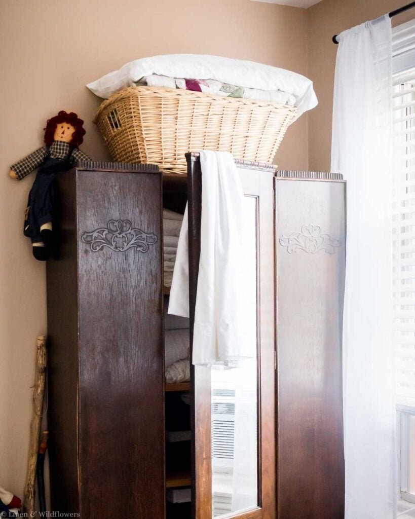 Vintage storage idea with a wicker basket of linens on top of an antique wood armoire.