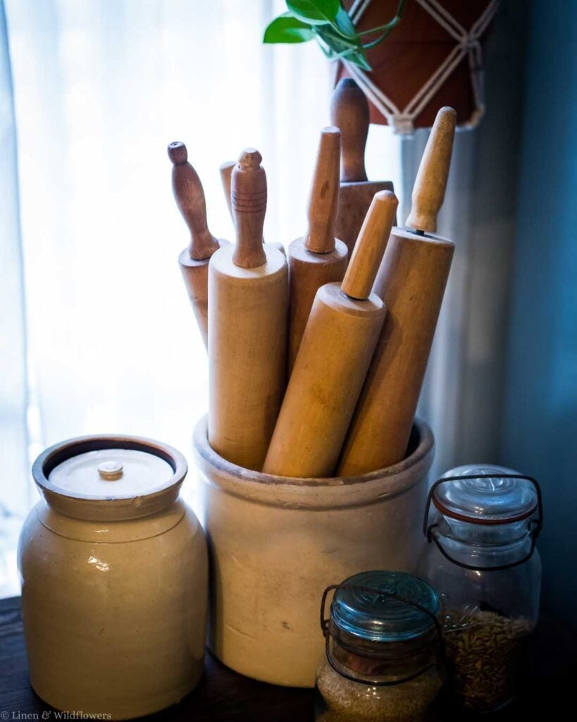 Vintage storage idea displaying a collection of wooden rolling pins inside an antique stoneware crock.