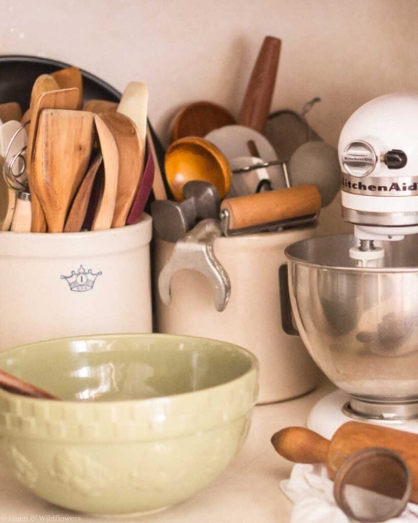 Vintage storage idea using stoneware crocks to organize wooden kitchen utensils on a farmhouse counter.