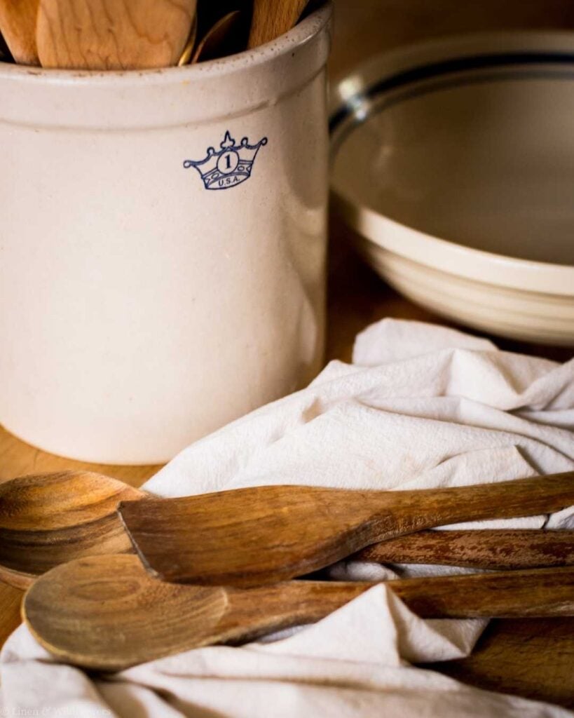 Wooden spoons resting on linen in front of a vintage stoneware crock, illustrating proper wooden utensil care.