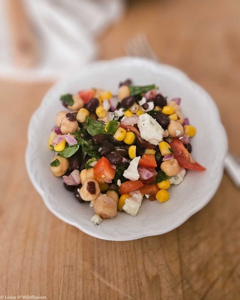 Small white bowl of chickpea salad with lemon topped with crumbled blue cheese.