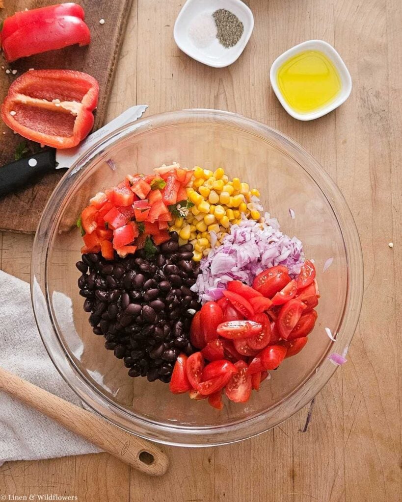 Black beans, chickpeas, corn, diced tomato, and red onion in a glass bowl before mixing.