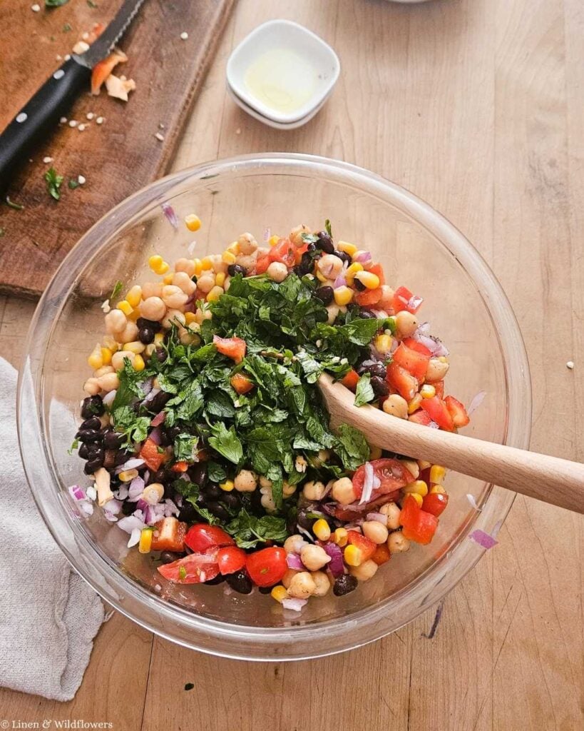 Chopped parsley being mixed into chickpea salad with lemon in a glass bowl.