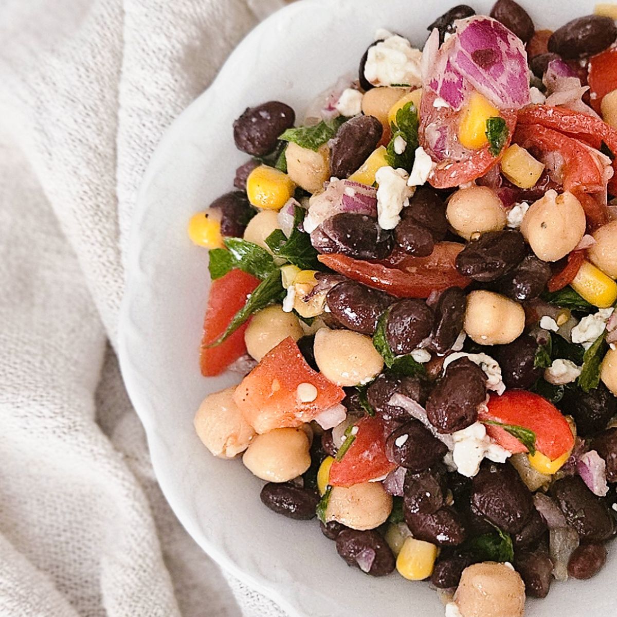 Chickpea salad with lemon, black beans, tomato, red onion, corn, and feta in a white bowl.