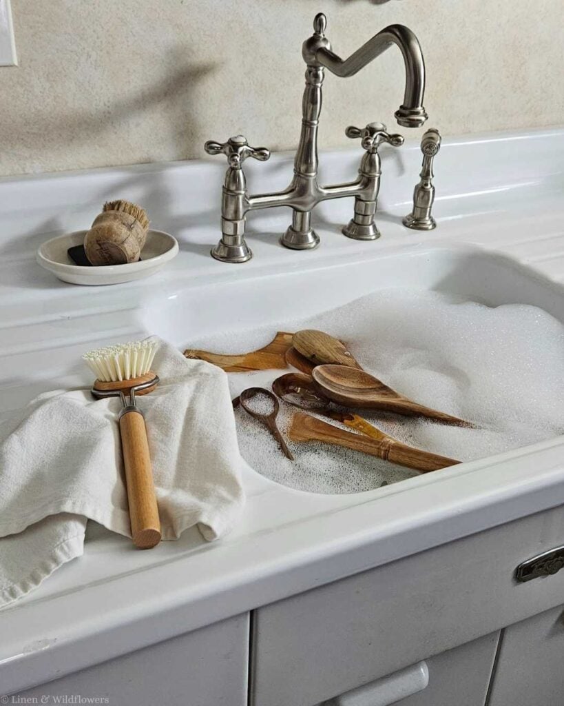 Wooden spoons and spatulas soaking in a sink full of soapy water, illustrating a common mistake that ruins wooden utensils.