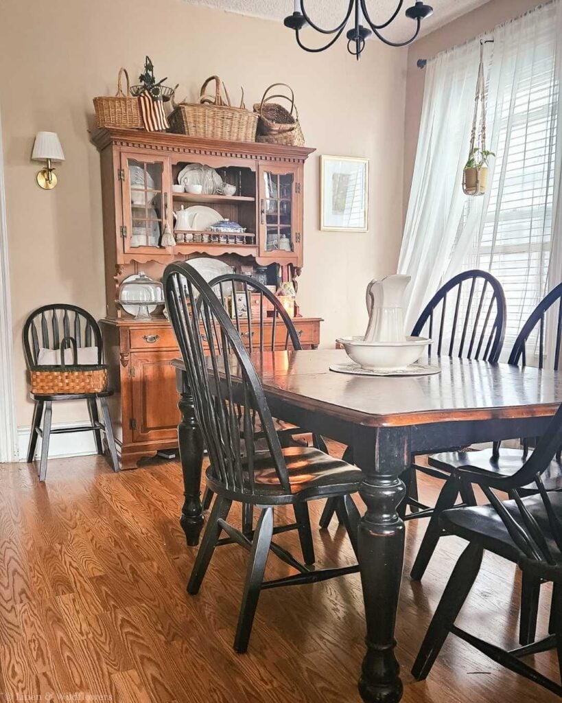 Assorted vintage wicker baskets arranged on top of a wooden hutch in a farmhouse dining room.