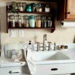 Budget-friendly farmhouse kitchen with vintage mason jar spice shelf, apron sink, and bridge faucet — cozy cottage kitchen decor ideas.