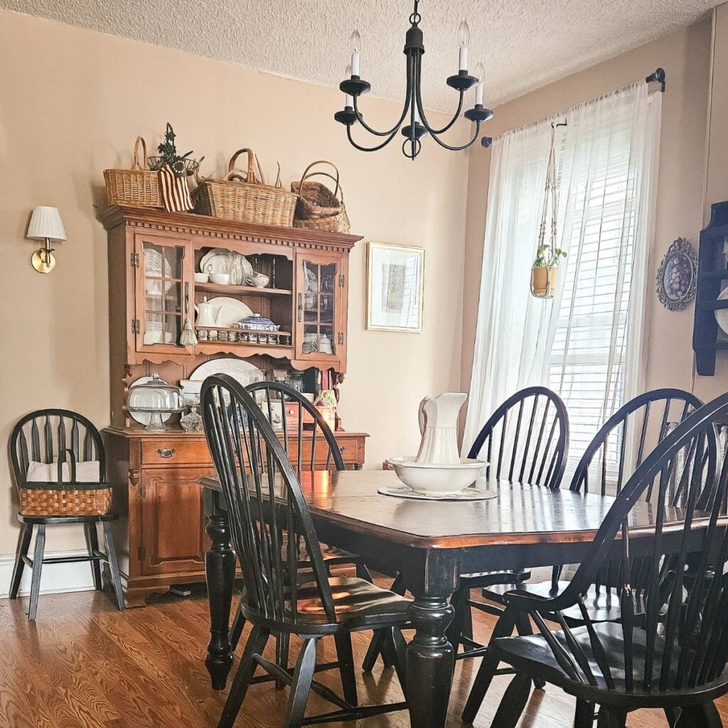 Vintage wicker baskets styled on top of a farmhouse dining room hutch surrounded by black windsor chairs.