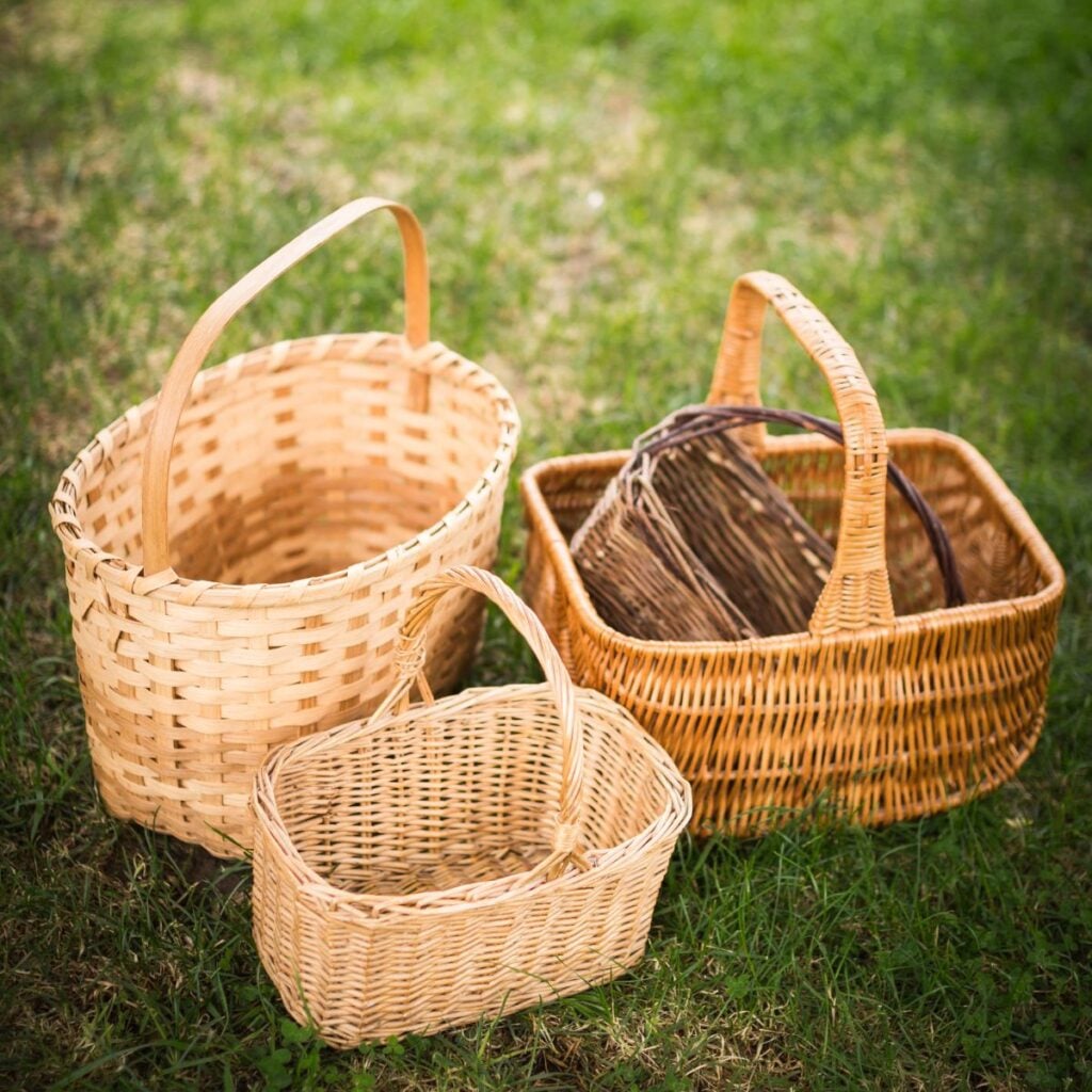 Four vintage wicker baskets of varying shapes and sizes sitting in green grass, ready for cleaning.