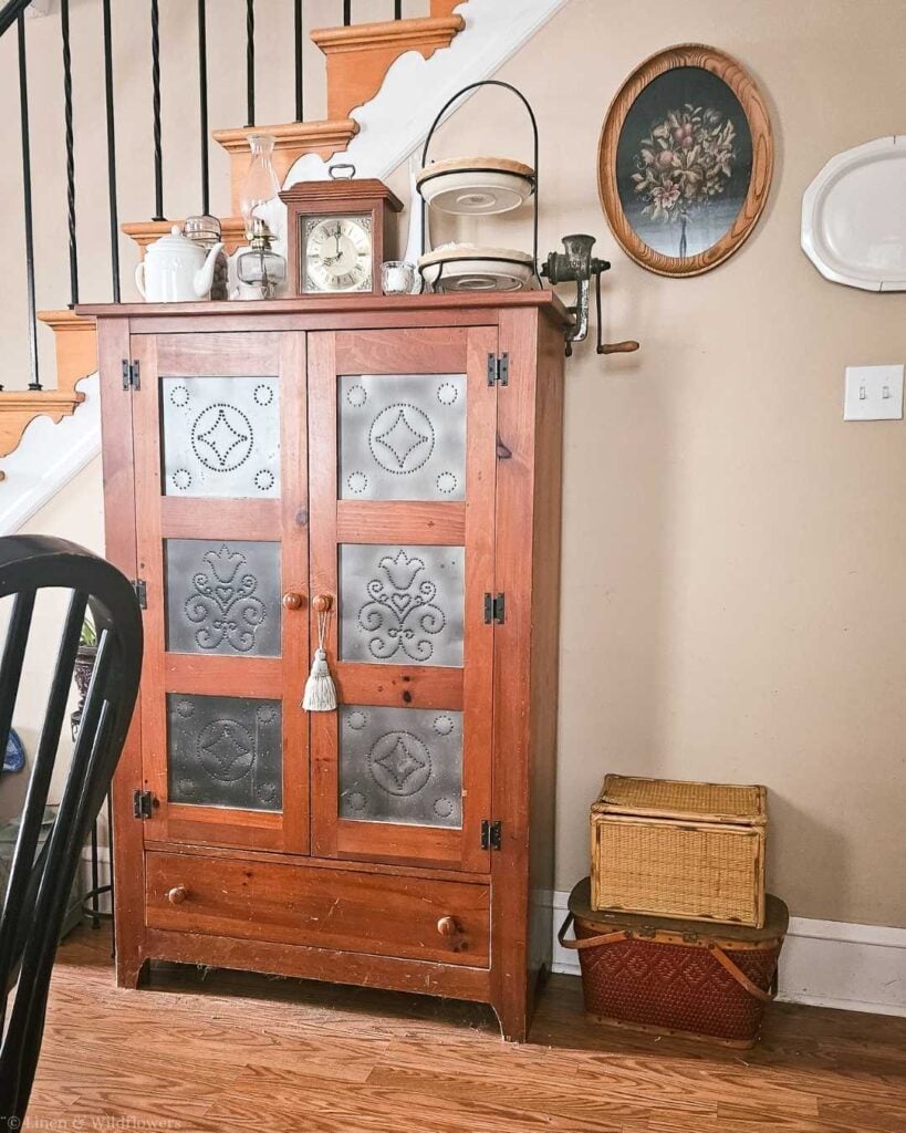 Vintage wicker picnic baskets stacked next to an antique punched tin pie safe in a farmhouse entryway.