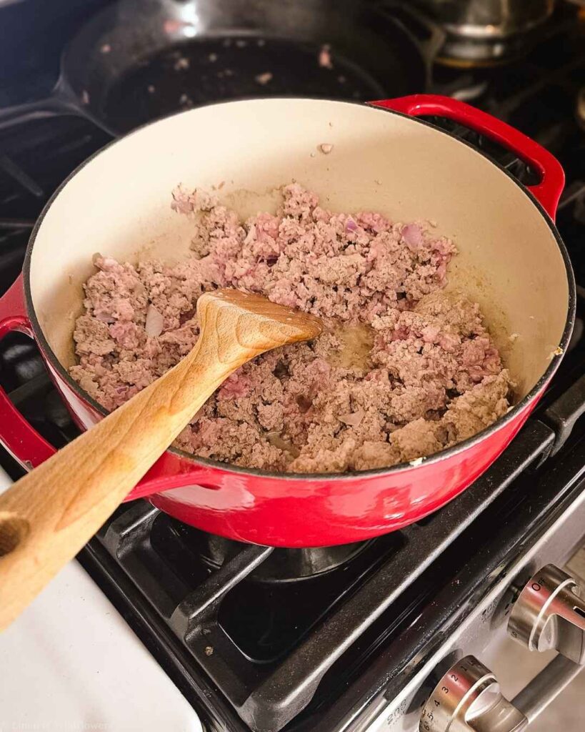 Ground turkey and onion browning in a red Dutch oven for homemade turkey lasagna.