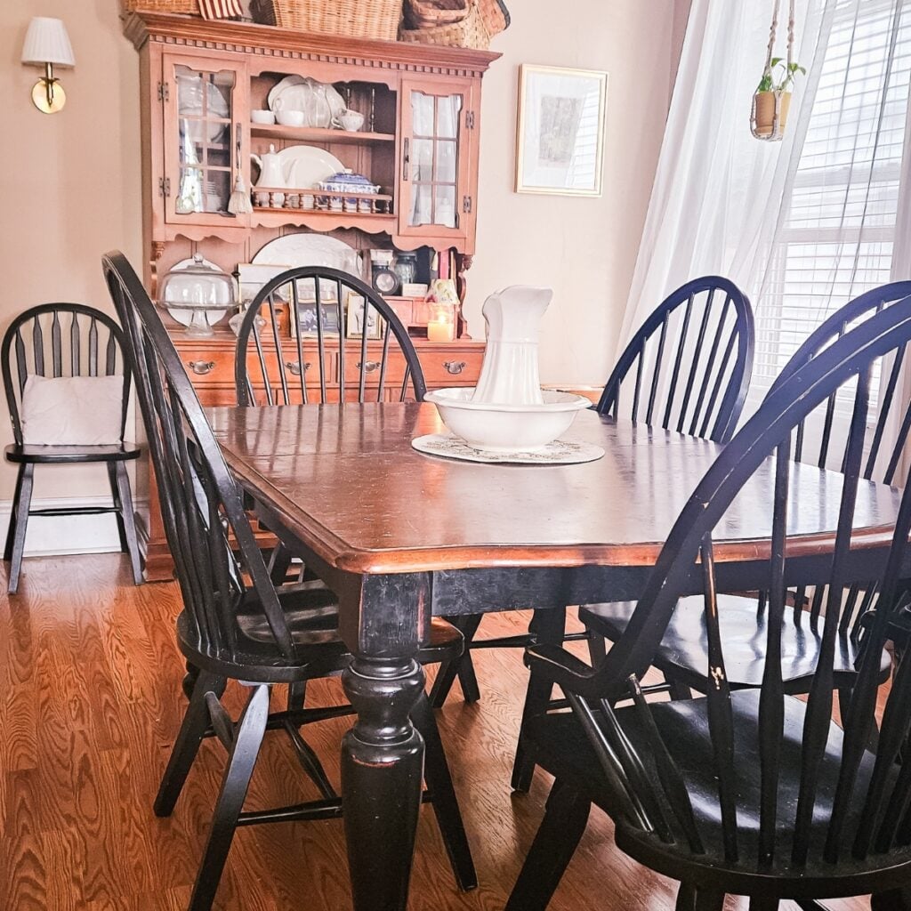 Country farmhouse dining room with black Windsor chairs, thrifted table and antique hutch.