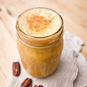 Easy pumpkin pie smoothie in a mason jar topped with cinnamon, with pecans and a linen towel on a wooden board.
