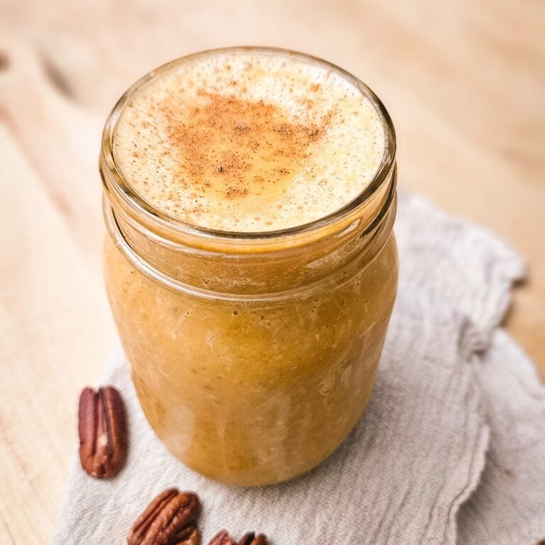 Easy pumpkin pie smoothie in a mason jar topped with cinnamon, with pecans and a linen towel on a wooden board.